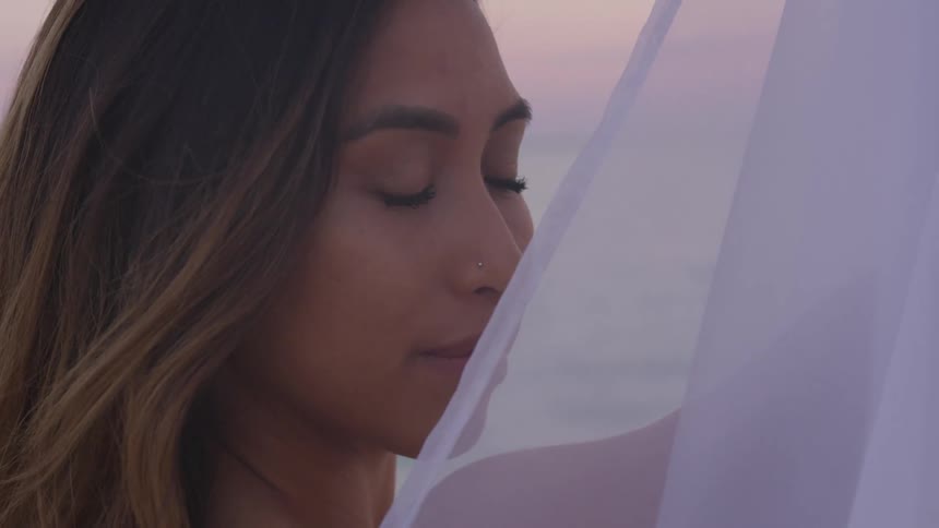 A woman outside holds sheer material up by her face