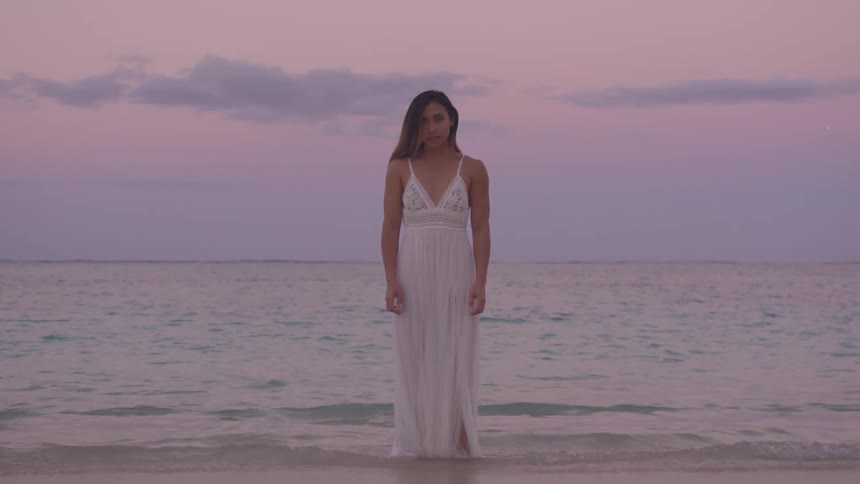 A woman is wearing a dress and standing at the beach