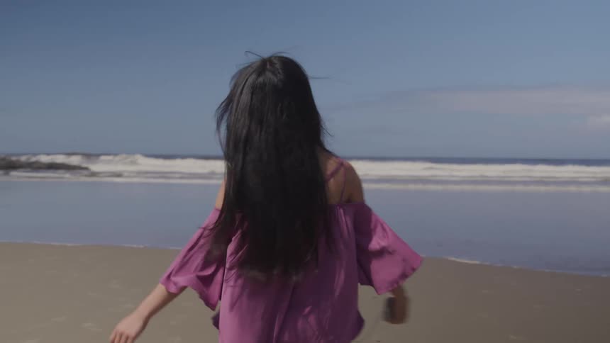 A teenage girl with headphones in dances on the beach