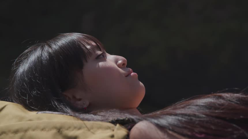A woman with earrings laying down and blinking with light shining on her