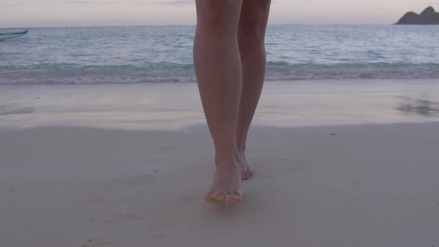 A woman walks on the beach in opposite direction of the ocean
