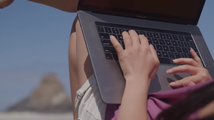 A woman is typing on a laptop outdoors
