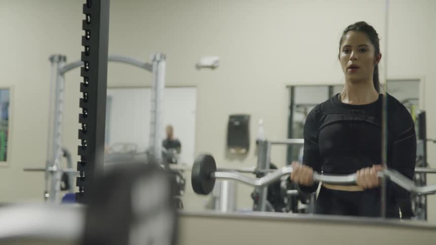 Young woman lift weight in a gym while looking at the mirror
