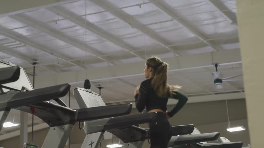 A young woman runs on a treadmill inside of a gymnasium