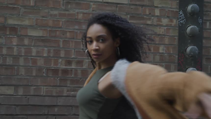 Young black woman dances in front of brick wall