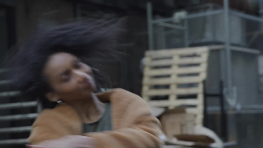 A young woman dances in an alleyway in a city during the day