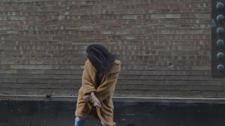 A young black woman dances in an alleyway in a city during the day