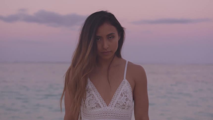 A young woman standing on a beach moves her head up and looks forward