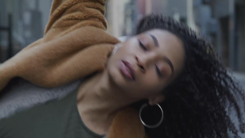 A young black woman dances in an alleyway in a city while looking into the camera