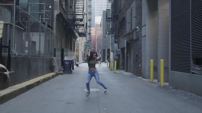 A teenage girl dances in an alley as people and cars go past