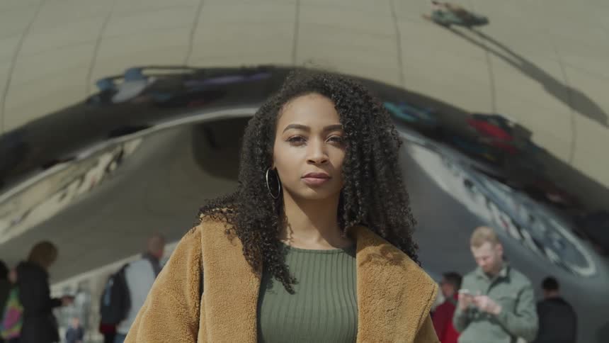 A woman with a jacket a sweater and earrings standing with people in the background