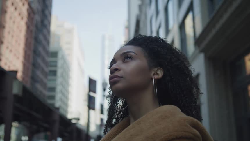 A woman stands on an inner city street while staring upward