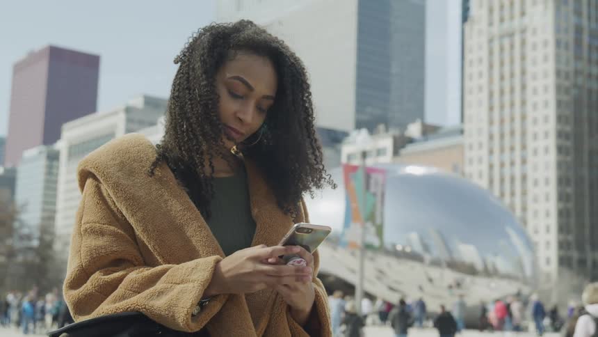 A woman at a tourist destination scrolls on her cell people as people walk behind her