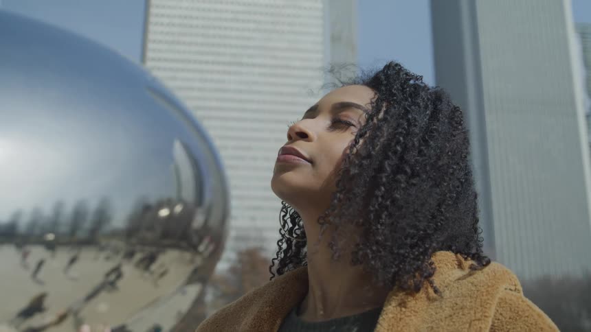 Young woman stands with eyes closed in front of cloudgate in chicago