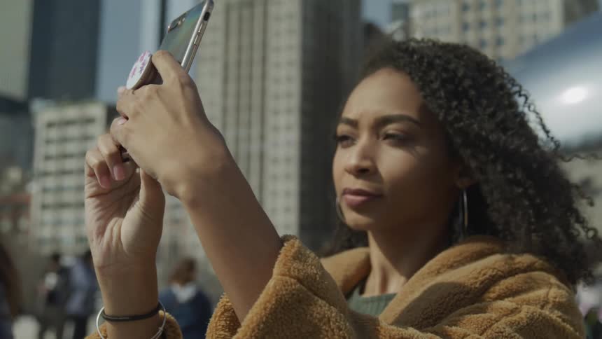 A woman takes a selfie with her phone at a tourist spot in a city as other pedestrians walk around