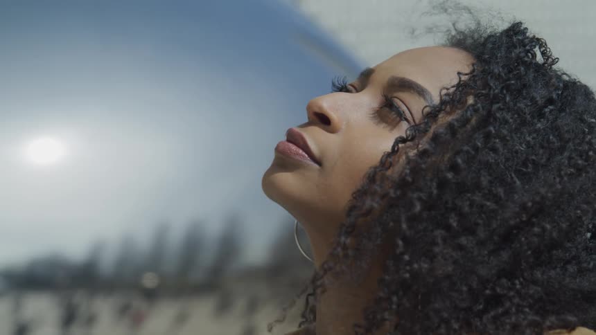 Side view of a woman with curly hair and hoop earrings looking up at the sky on a sunny day