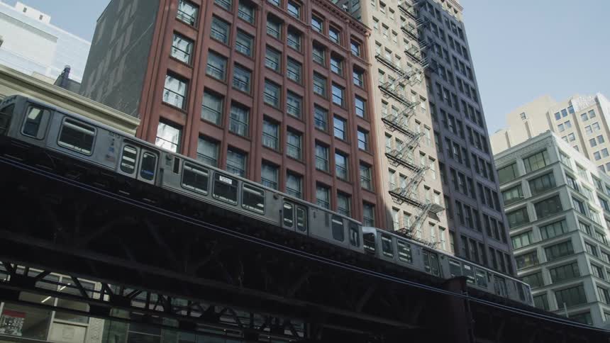 A train moving on a train track with buildings and windows the sky and clouds in the background