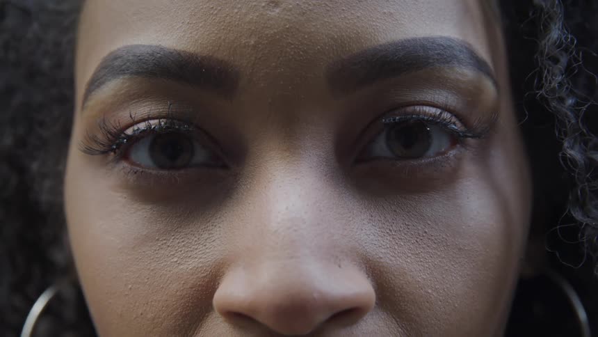 Black woman with curly hair and hoop earrings stares at the camera