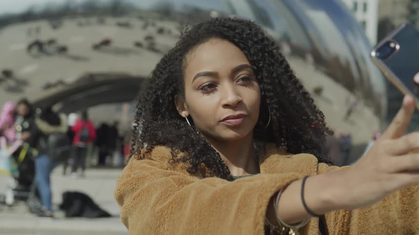 Young woman taking selfie in front of cloud gate sculpture in chicago