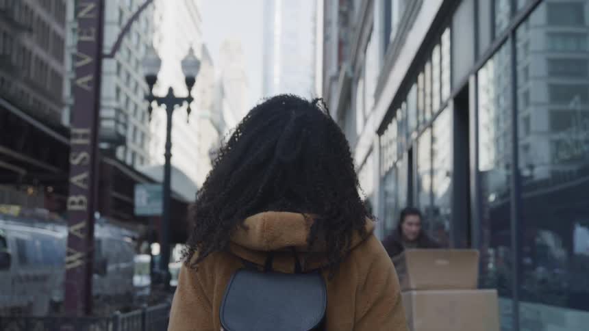A woman with a backpack walking in a city surrounded by buildings