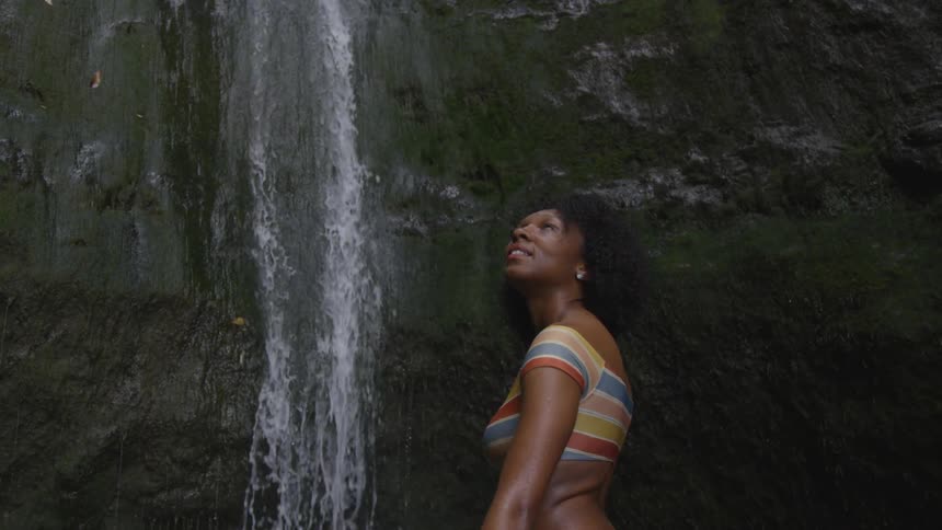 A young black woman looks at a waterfall going over a canyon