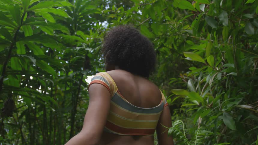 A black woman walks through a forest thick with vegetation