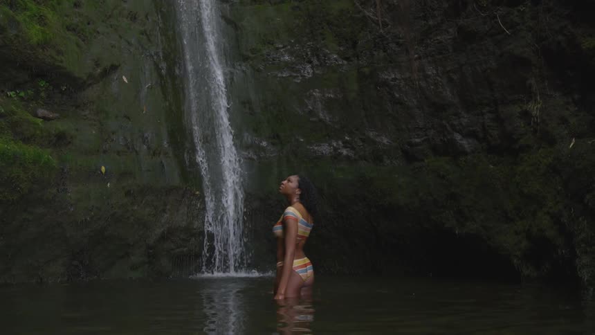 A teenage girl standing in a river watching a waterfall