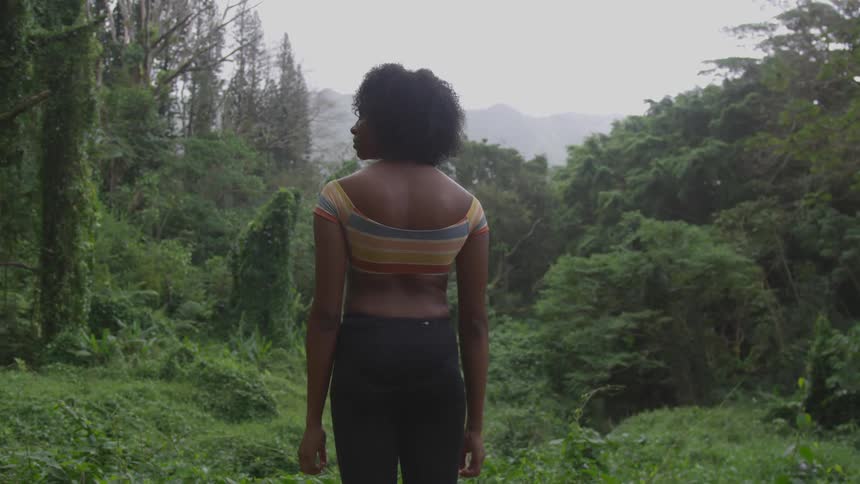 A teenage girl stands in a forest as rain falls down