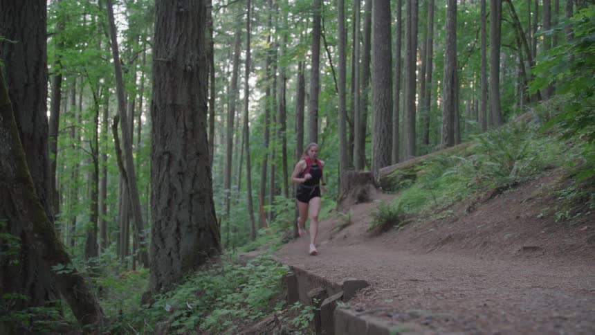 A woman is jogging outdoors in a forest