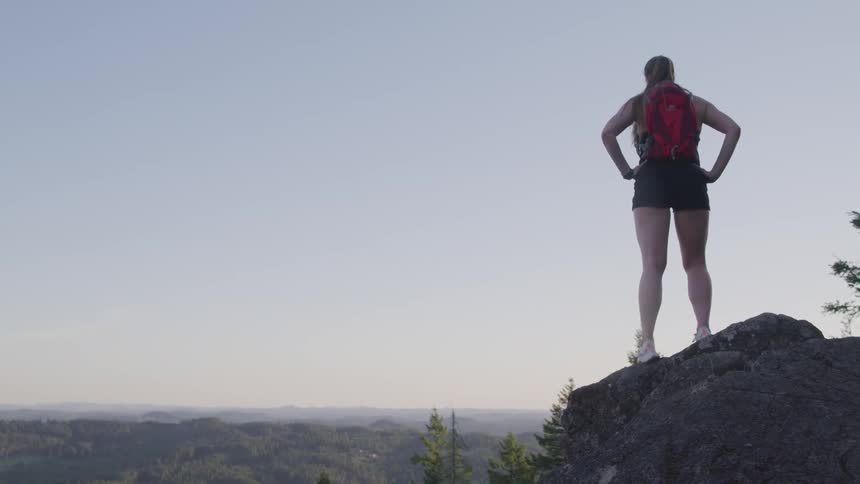 Woman stands on rock above landscape looking towards horizon