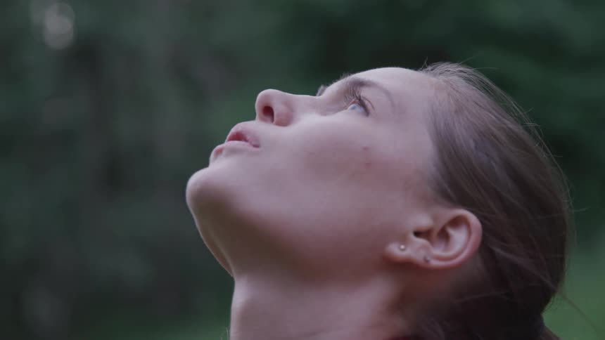 Side view of a woman with a ponytail and earrings looking up at the sky