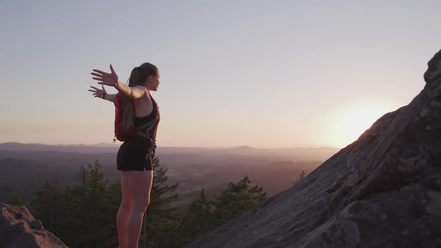 A woman is standing on the cliff with her arms reached out