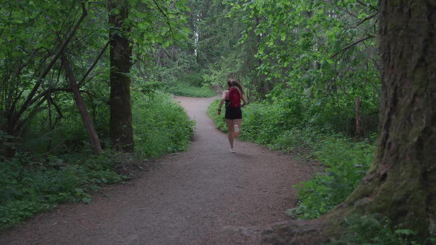 An athletic woman runs swiftly along a trail that pass through a forested area