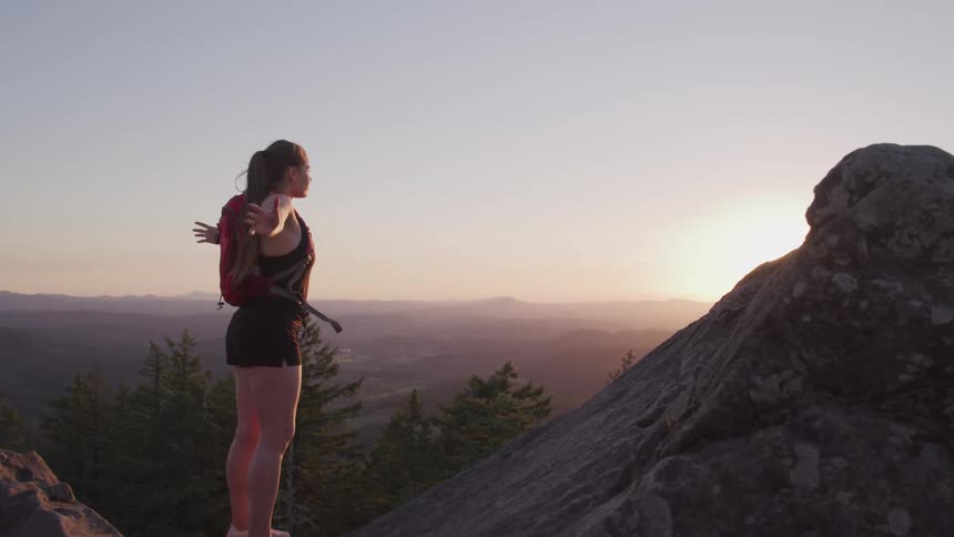 A woman stands on the summit of a canyon and holds her arms out