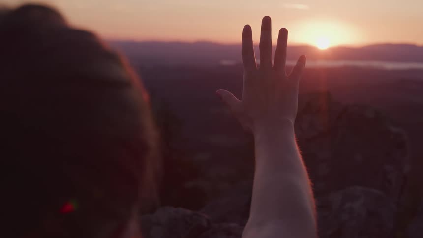 Sunset sunlight filtering through the fingers of a womans extended hand in the mountains