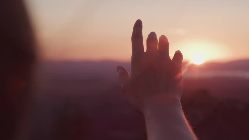 A woman holding out her hand with the sky clouds and a sunset in the background