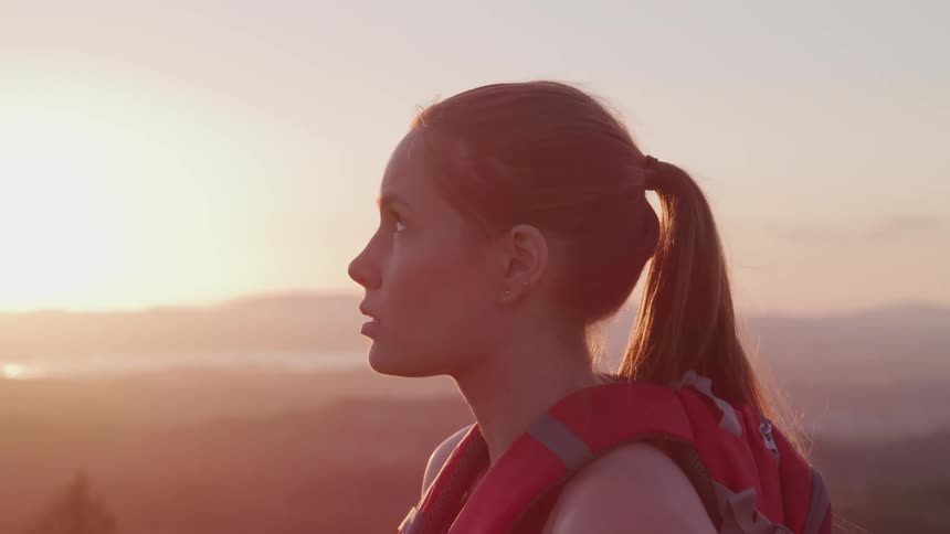 Young woman with backpack with mountains and sunrise in background