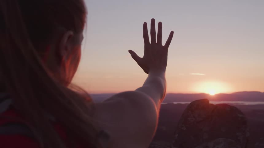 A woman stands with her arm extended towards the horizon as she looks at the landscape