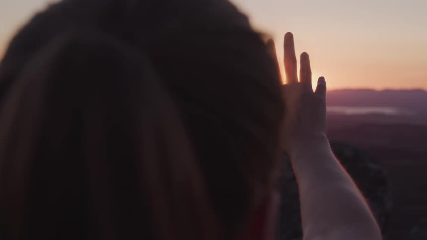 Woman facing sunset on horizon with hand raised