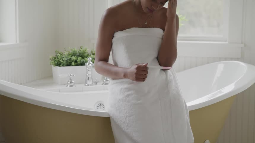 Woman sitting on edge of bathtub looking at pregnancy test