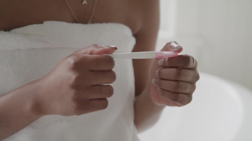 Young woman wearing a towel sits in the bathroom checking a pregnancy test