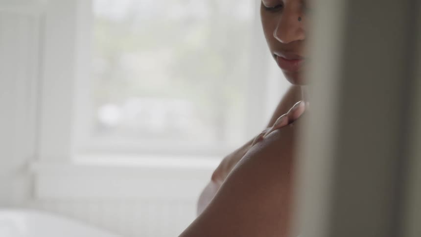 A woman sits in her bathroom in a towel and rubs her arm