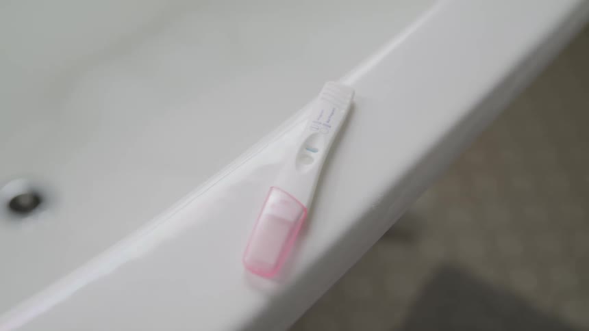 A pregnancy test sitting on the edge of a bath tub
