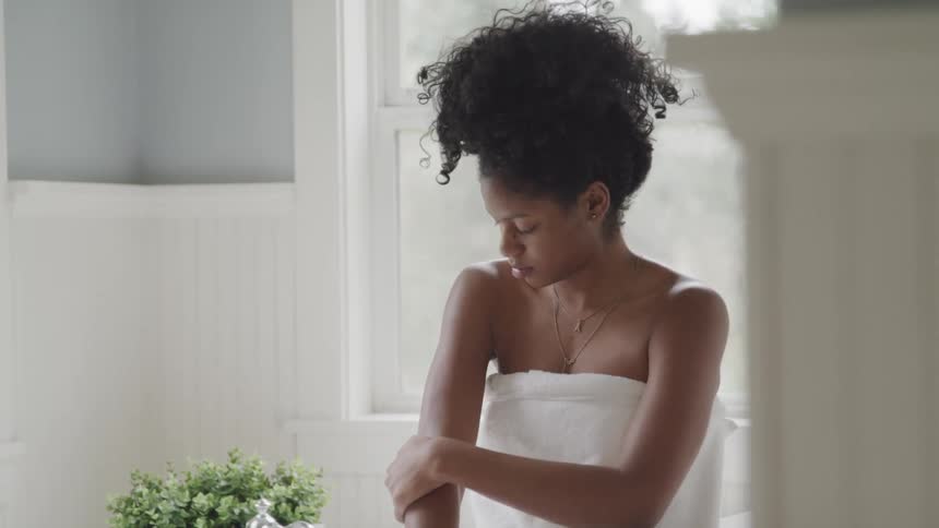 Young woman wearing a white towel rubs the skin of her hands sitting in the bathroom at home