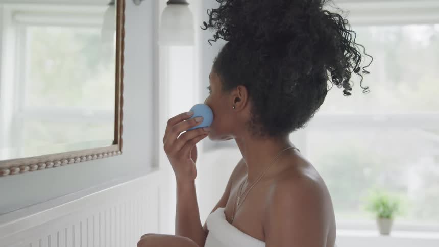 Young woman wearing a towel cleans makeup from her face in front of a mirror in the bathroom