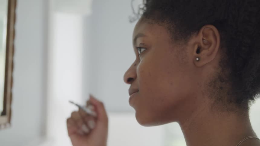 Young woman applies makeup to her eyebrow with a brush in front of a mirror in the bathroom
