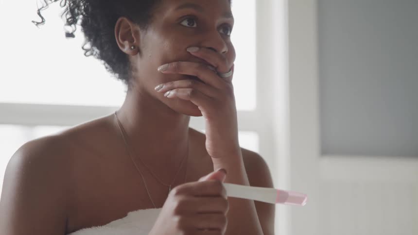 Young woman looks at pregnancy test in surprise then smiles