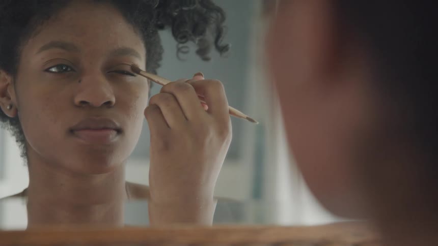 A woman is putting on makeup while looking in a mirror