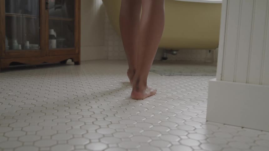 Barefoot person walks toward free standing bathtub