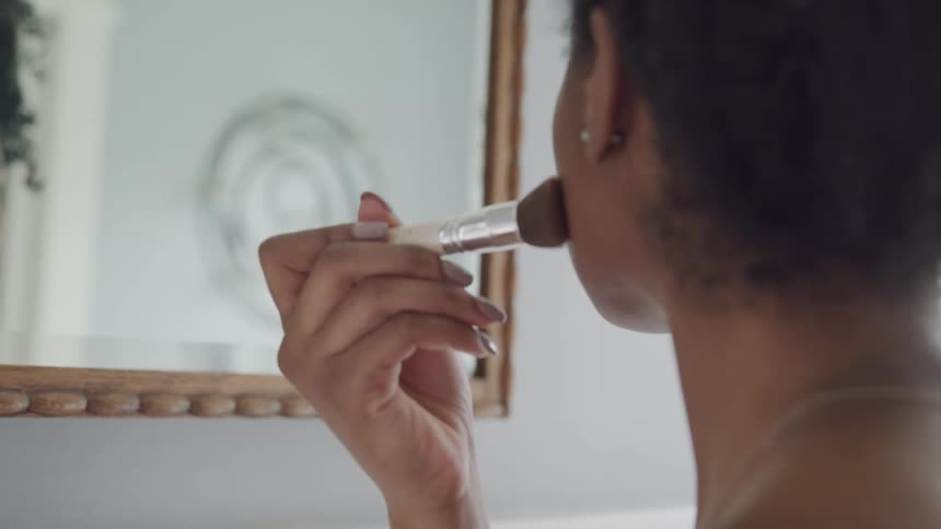 A woman is looking in a mirror and putting on makeup
